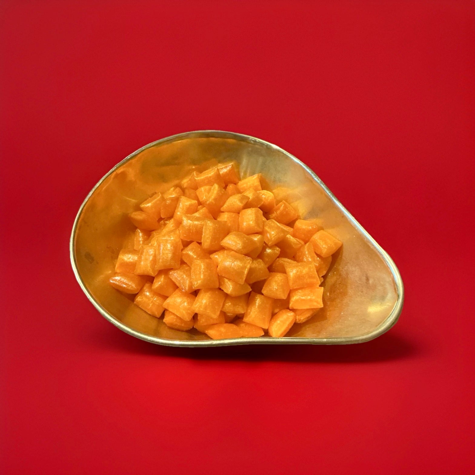 Hard boiled iron brew flavoured cushion shaped sweets in a gold bowl with a red background 