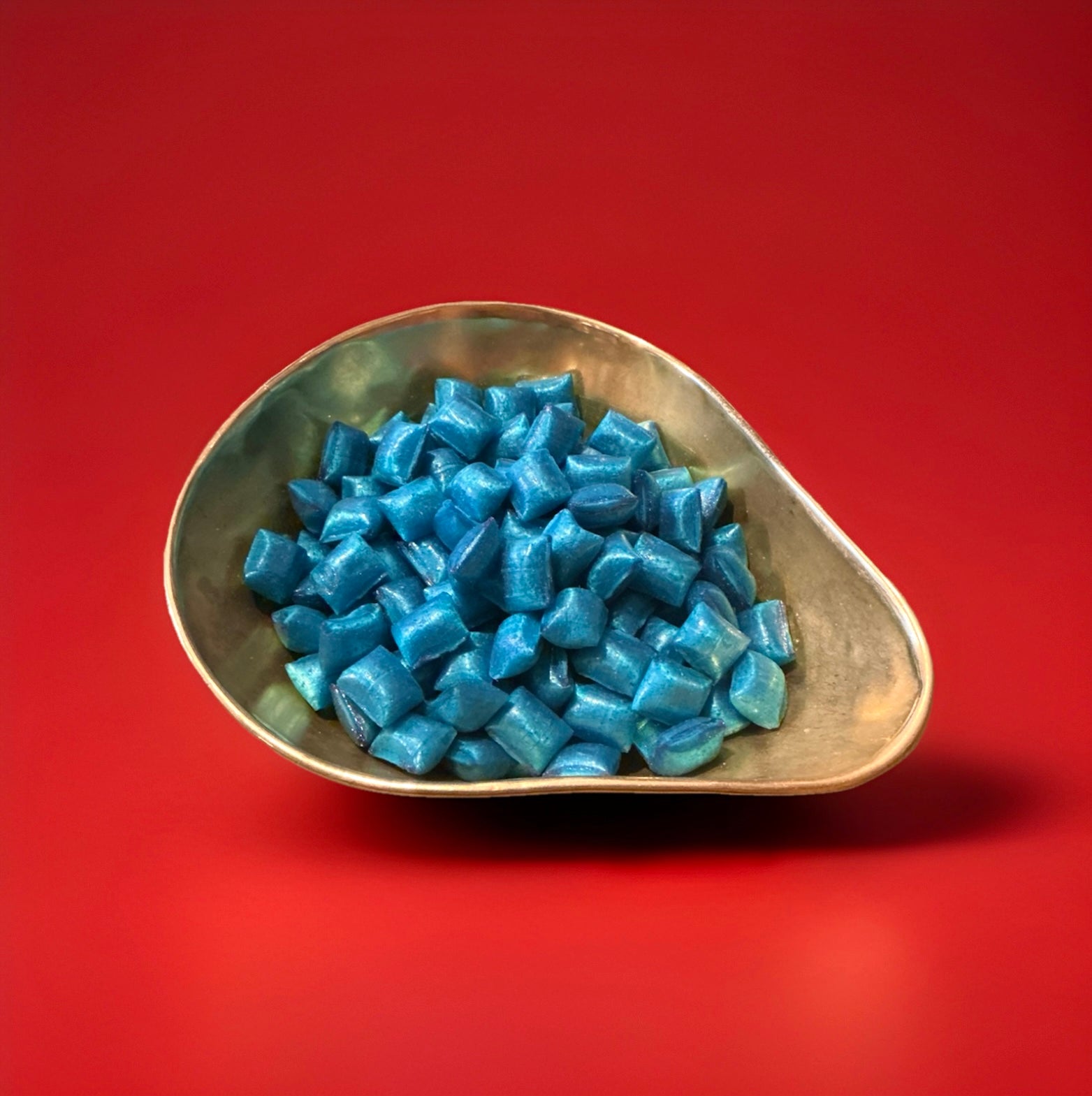 Blue raspberry flavoured hard boiled cushion shaped sweets in a gold bowl with a red background 