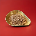 Brown coloured coconut strands coated in cocoa sugar in a gold bowl on a red background 