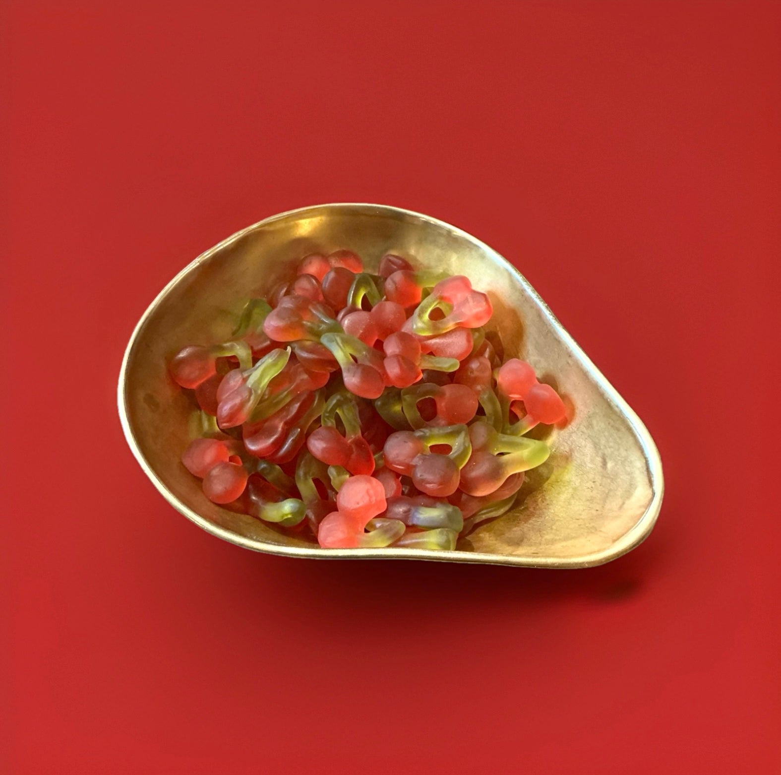Cherry shaped and cherry flavoured red and green jelly sweets in a gold bowl on a red background 