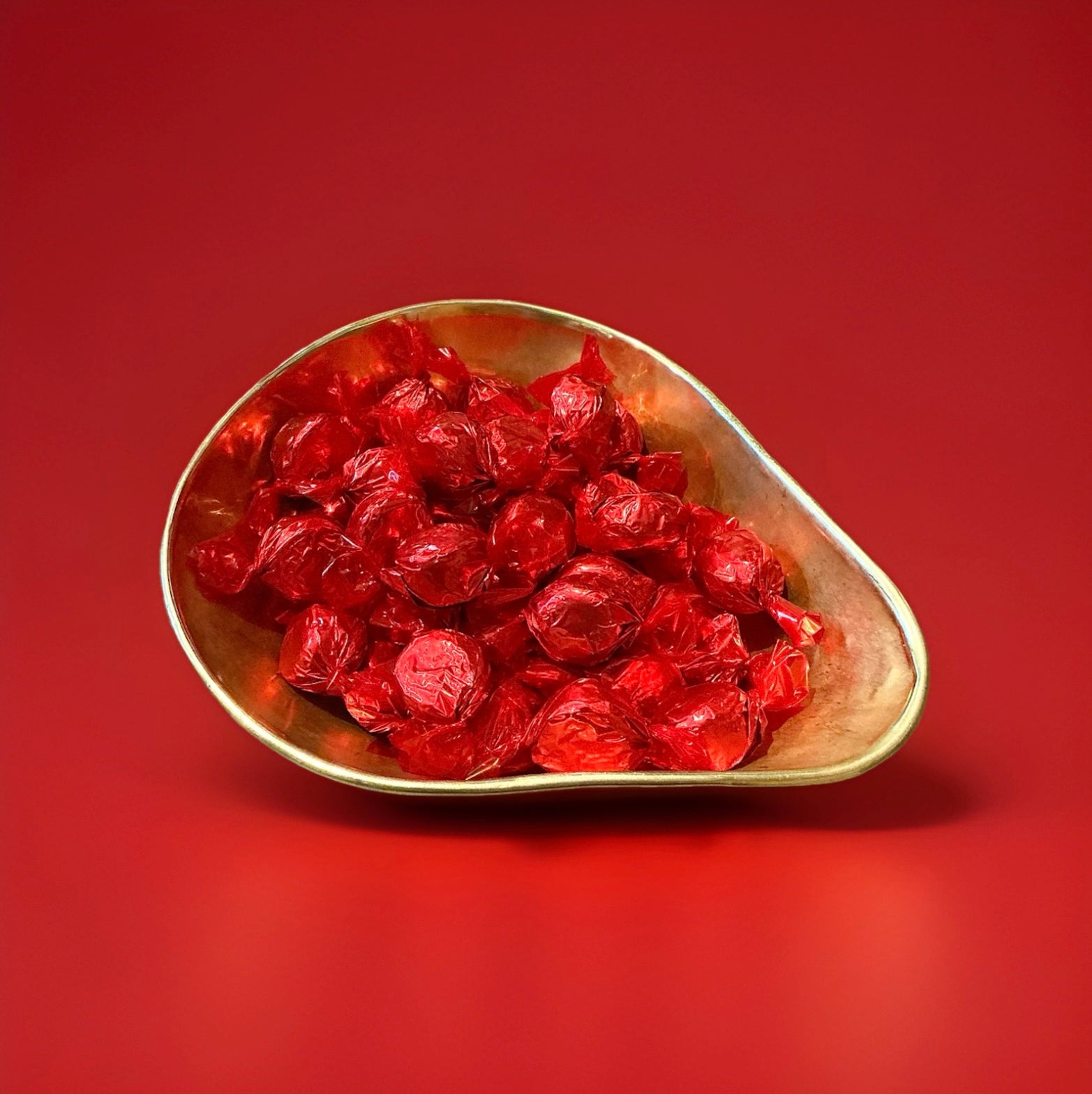 Individually wrapped red coloured raspberry and coconut sweets with a chocolate coating in a gold bowl on a red background 