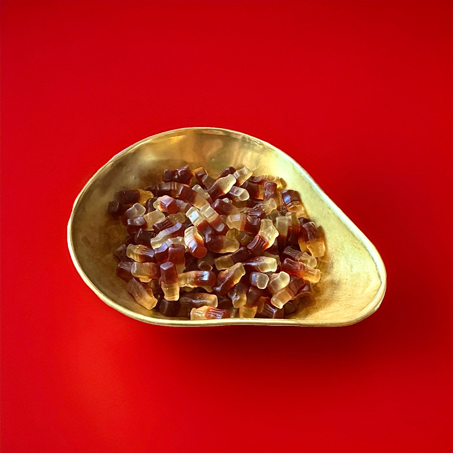 Brown and white cola bottle shaped and flavoured jelly sweets in a gold bowl on a red background 