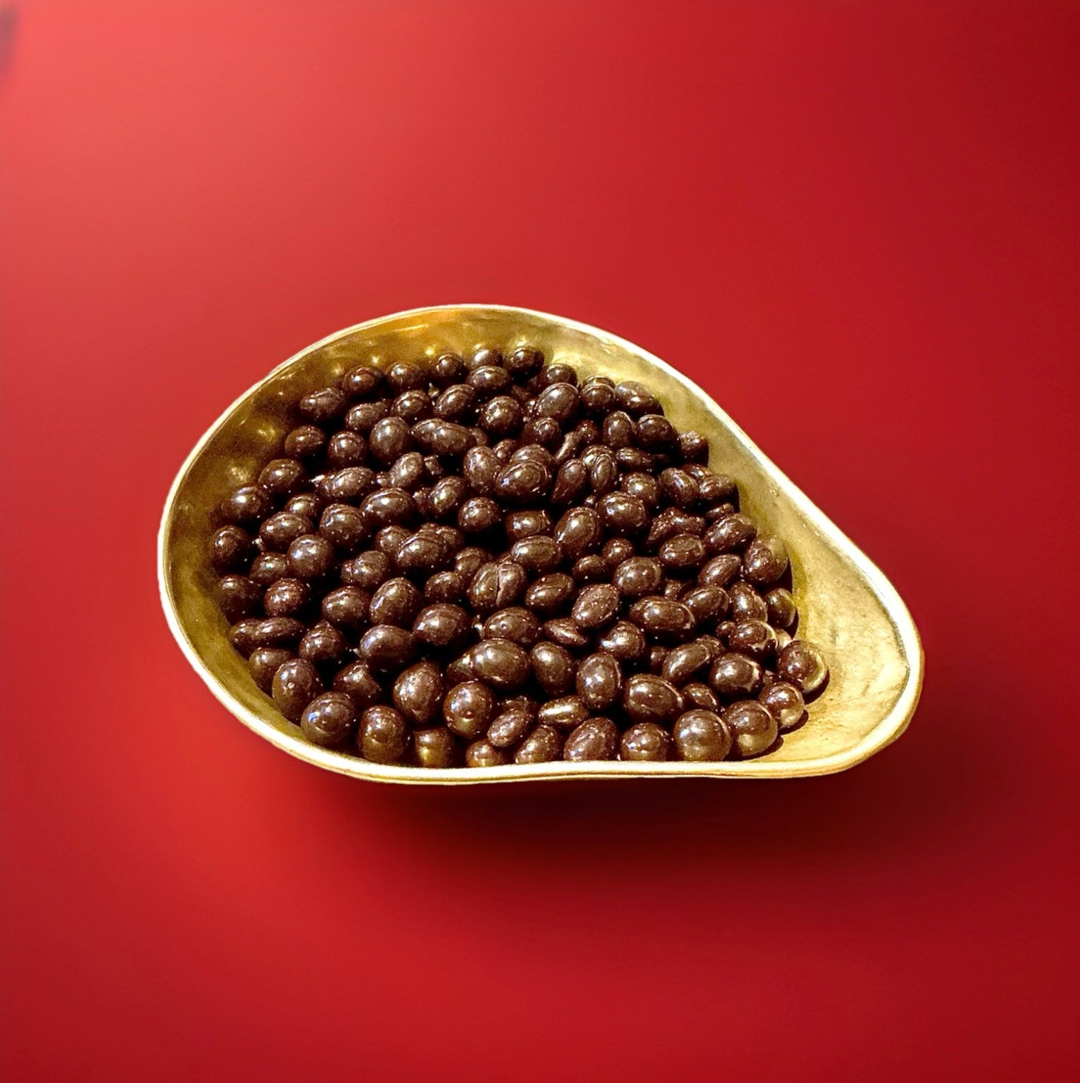 Peanuts coated in dark chocolate in a gold bowl on a red background 