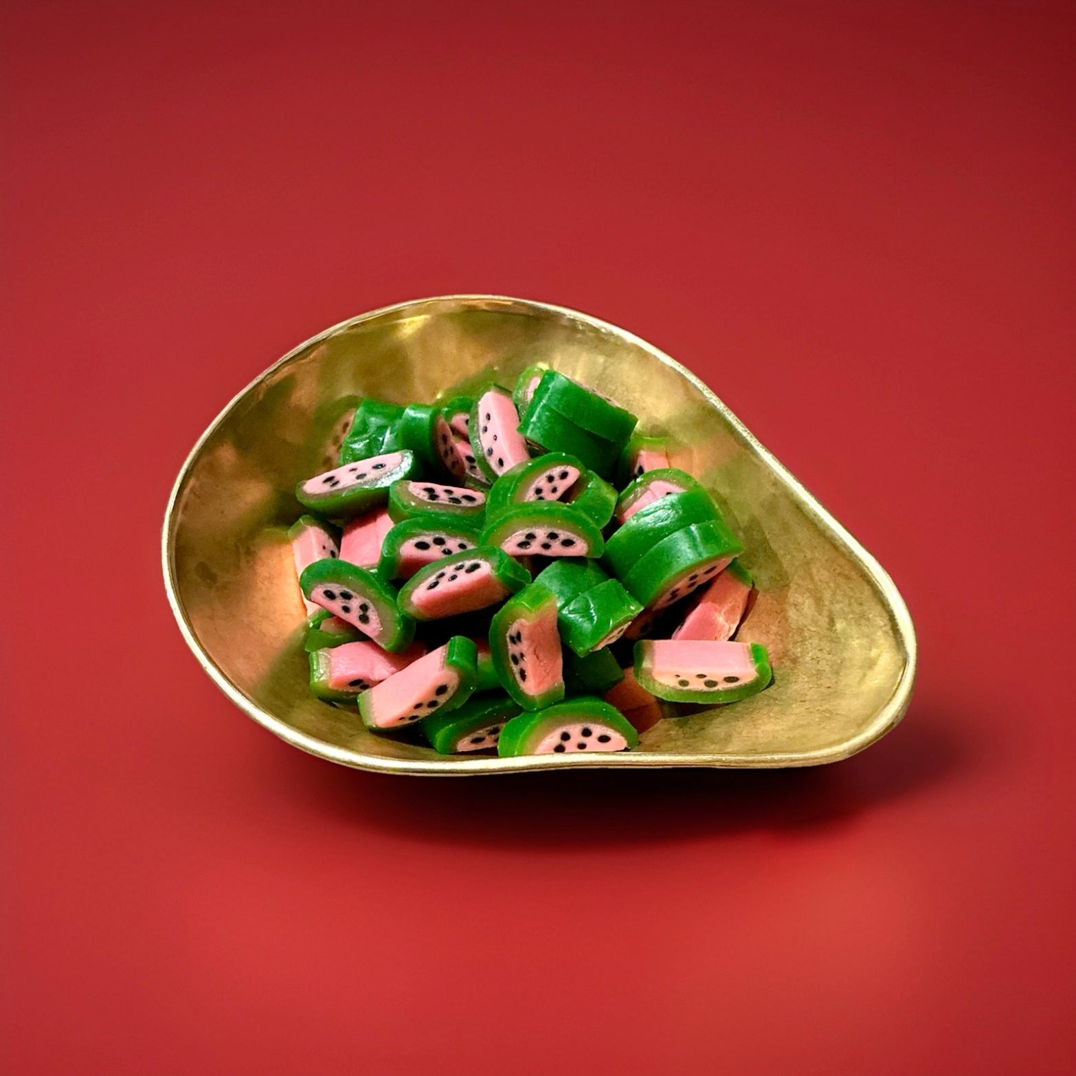 Green and pink watermelon shaped sweets in a gold bowl with a red background 