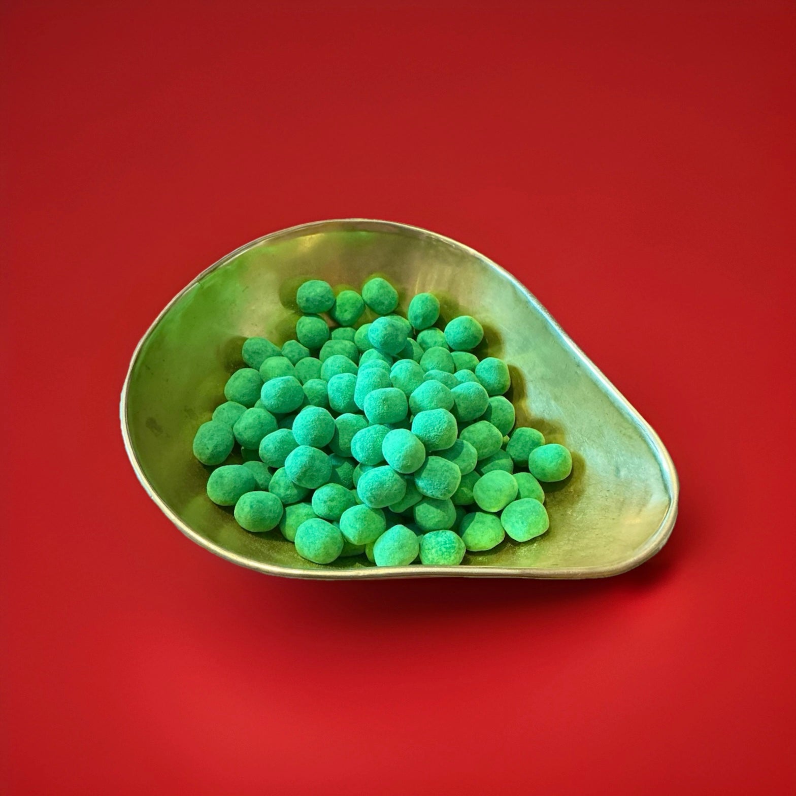 Round shaped bright Green coloured watermelon flavoured Bon Bon’s in a gold bowl on a red background 