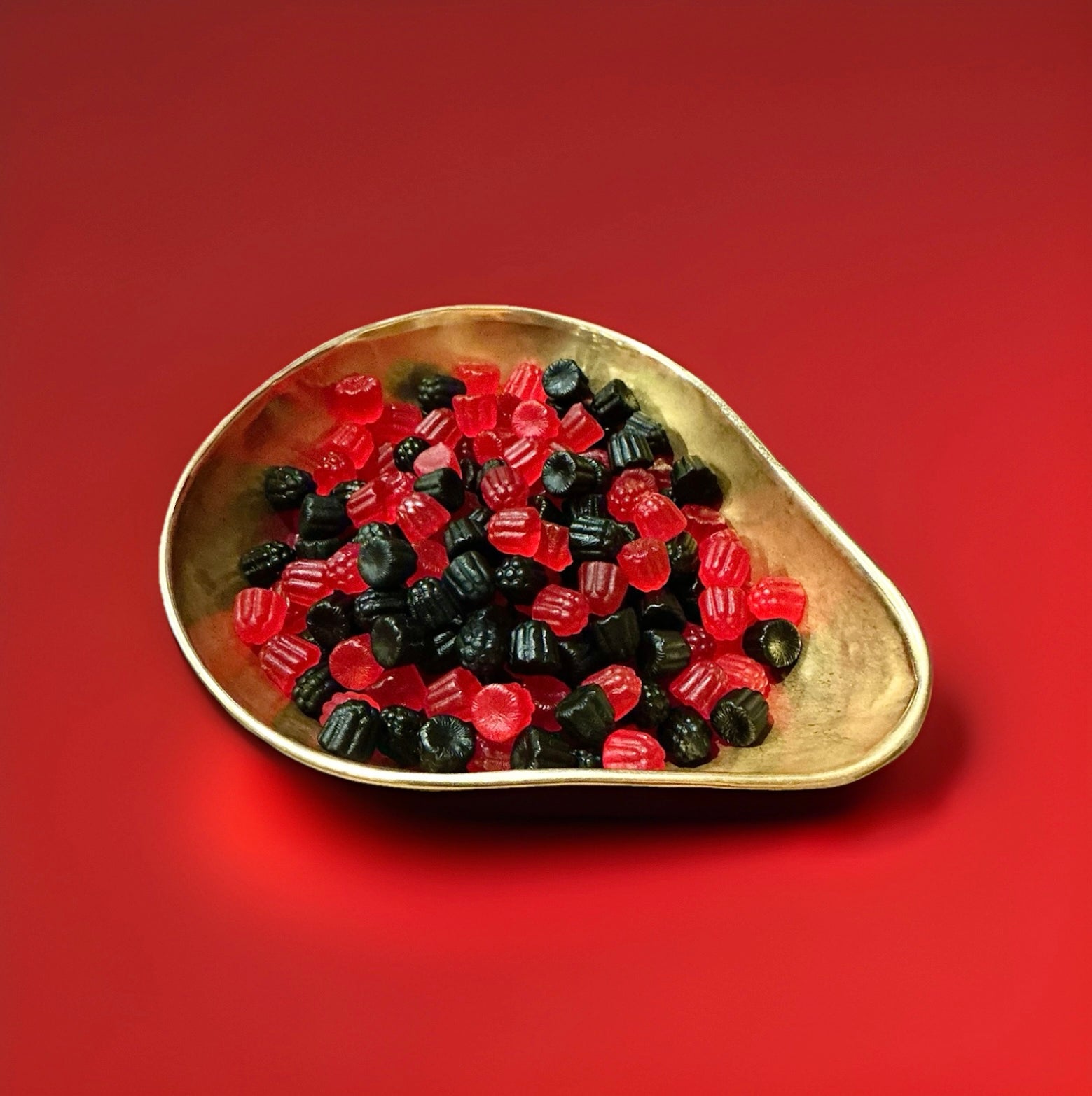 BlackBerry and Raspberry flavoured black and red coloured small hard gum jelly sweets in a gold bowl on a red background 