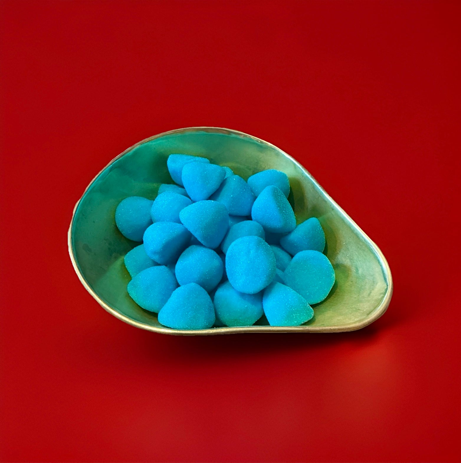 Bright blue marshmallows coated in sugar in a gold bowl with a red background 