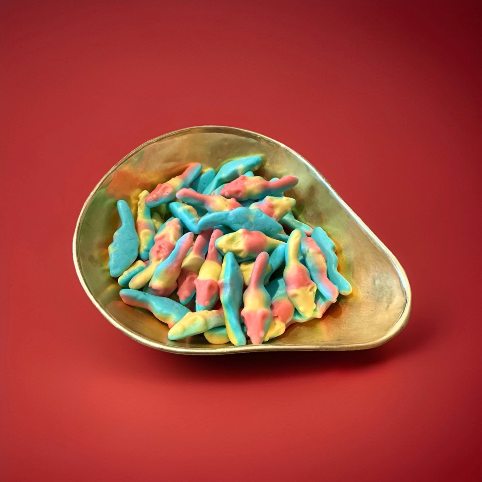 Multicoloured tutti fruity flavoured mouse shaped foam sweets in a gold bowl on a red background 