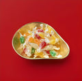 Individually wrapped multicoloured hard boiled pear flavoured sweets in a gold bowl on a red background 