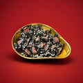 Individually wrapped black liquorice flavoured toffees in a gold bowl on a red background