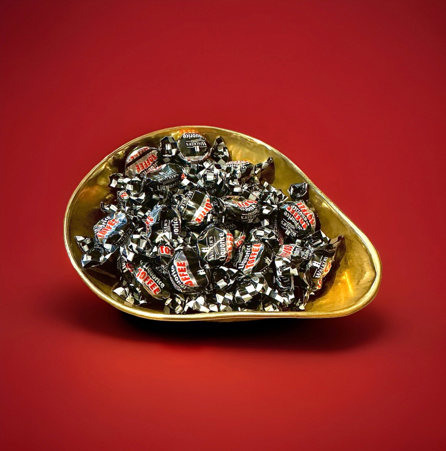 Individually wrapped black liquorice flavoured toffees in a gold bowl on a red background