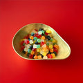 Multicoloured fruit flavoured mini gem jelly sweets in a gold bowl on a red background 