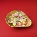 Red yellow and green Apple shaped jelly sweets with a sour sugar coating in a gold bowl with a red background 