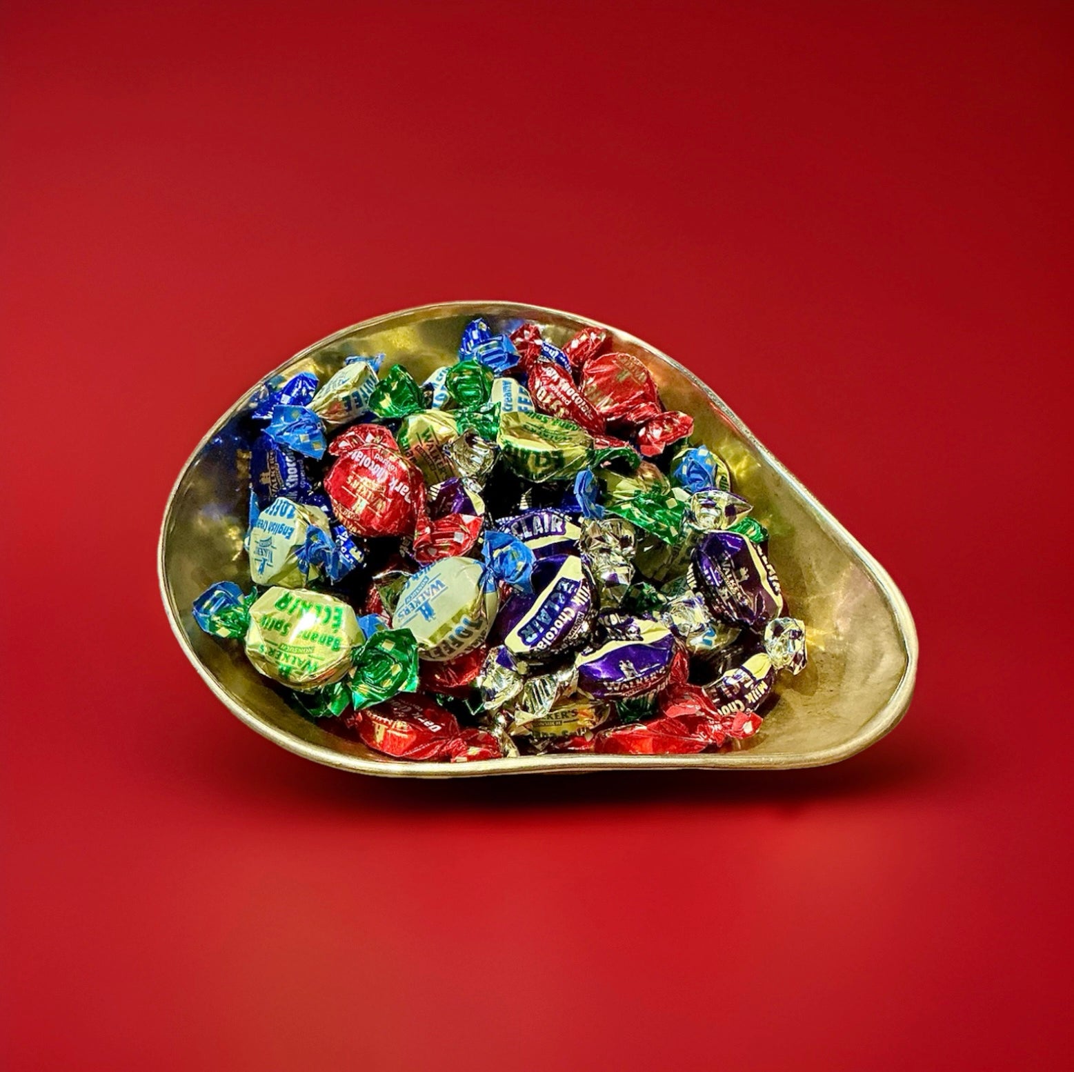 Individually wrapped assorted toffee flavours in a gold bowl on a red background 