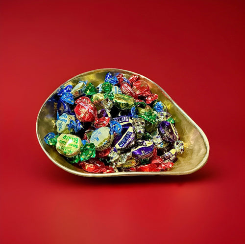 Individually wrapped assorted toffee flavours in a gold bowl on a red background 
