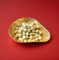 Bite sized pieces of mildly salted black liquorice coated in white chocolate in a gold bowl with a red background 