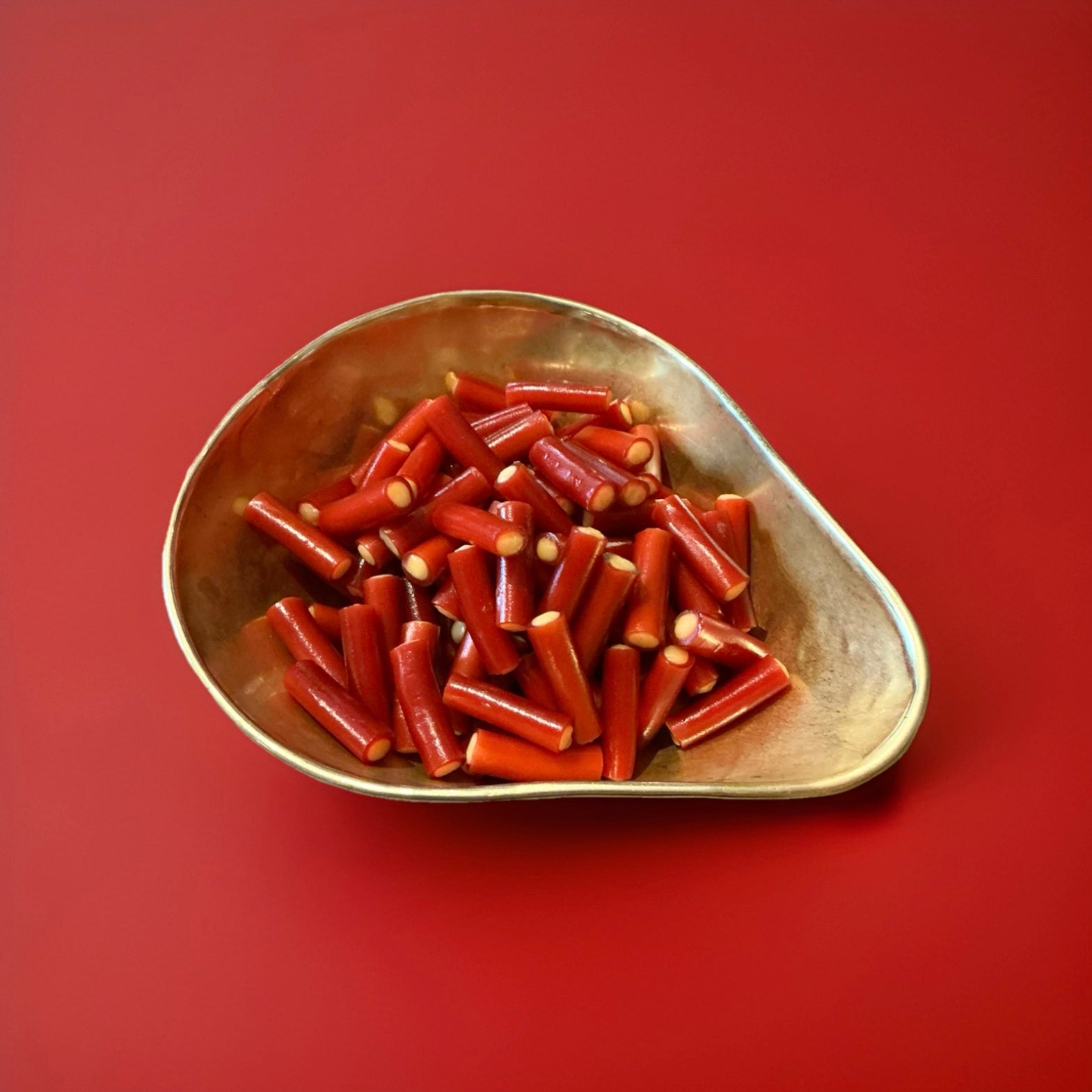 Red coloured rhubarb flavoured liquorice tube with a yellow fondant centre in a gold bowl on a red background 