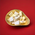 Yellow and pink coloured vanilla flavoured sherbet blocks in a gold bowl on a red background 