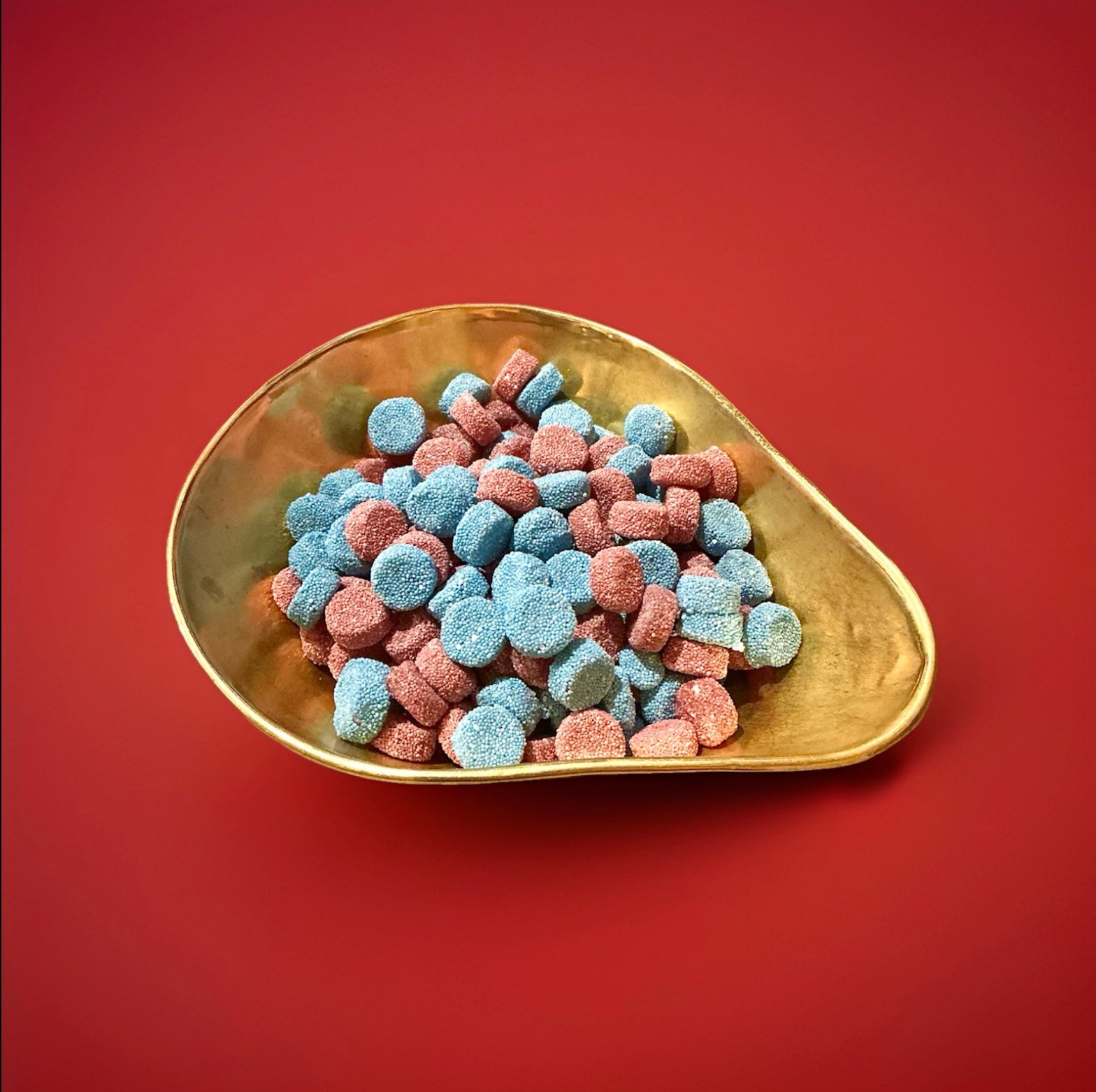Pink and blue aniseed flavoured jelly Spogs in a gold bowl on a red background 