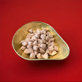 Bud shaped and cinnamon flavoured chewy sweets in a gold bowl with a red background 