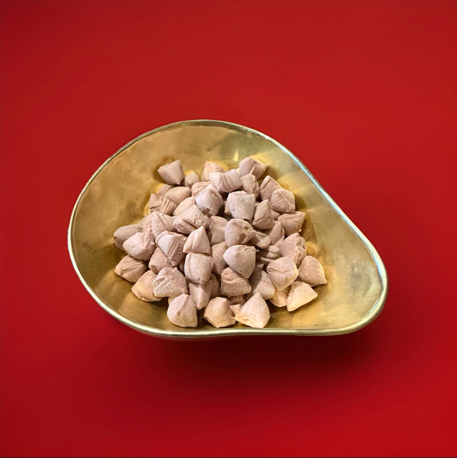 Bud shaped and cinnamon flavoured chewy sweets in a gold bowl with a red background 