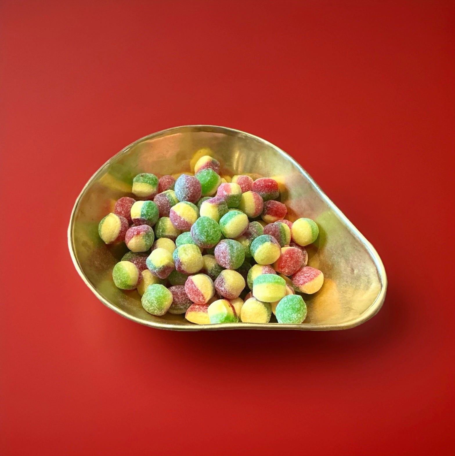 Red yellow and green hard boiled Rosie apple sweets in a gold bowl on a red background 