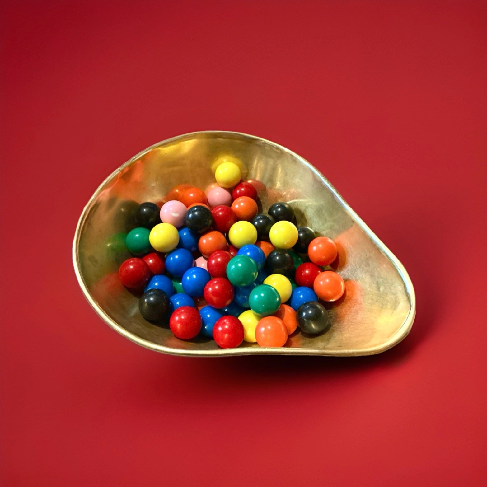 Multicoloured small round gob stoppers in a gold bowl on a red background 