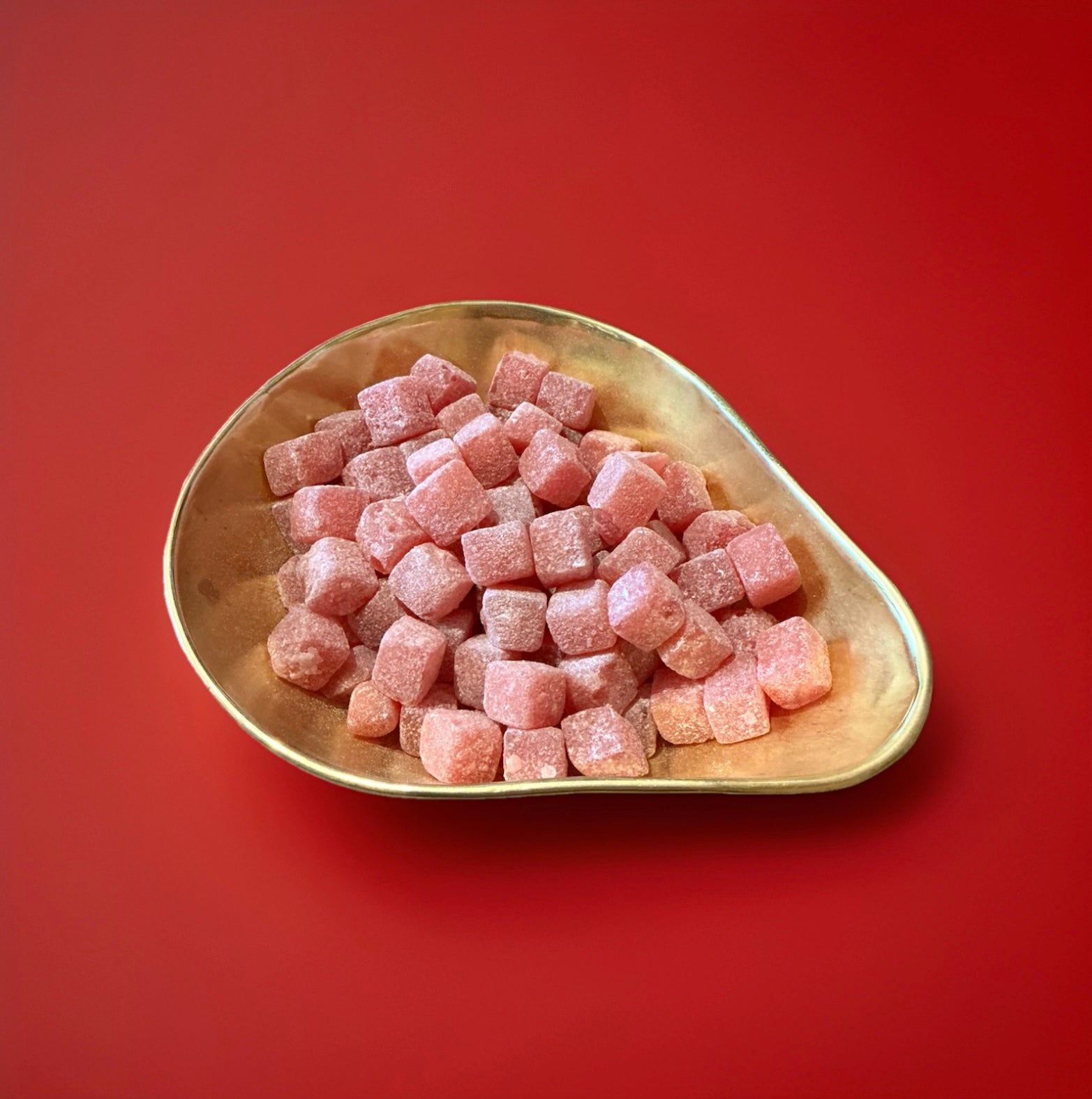 Red hard boiled soft centred cola cubes in a gold bowl with a red background 