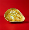 Pale yellow coloured individually wrapped hard boiled acid drop sweets in a gold bowl on a red background 