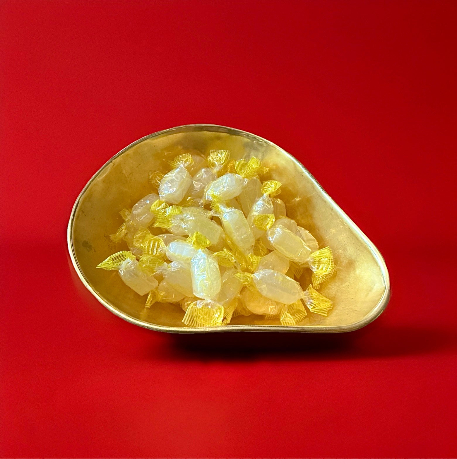 Pale yellow coloured individually wrapped hard boiled acid drop sweets in a gold bowl on a red background 