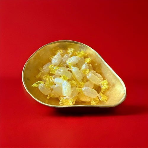 Pale yellow coloured individually wrapped hard boiled acid drop sweets in a gold bowl on a red background 