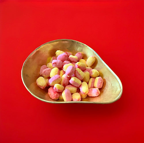 Oval half pink half yellow hard boiled rhubarb and custard sweets in a gold bowl with a red background 