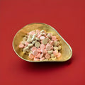 Brown and pink coloured chalky discs with a floral and violet flavour in a gold bowl with a red background 