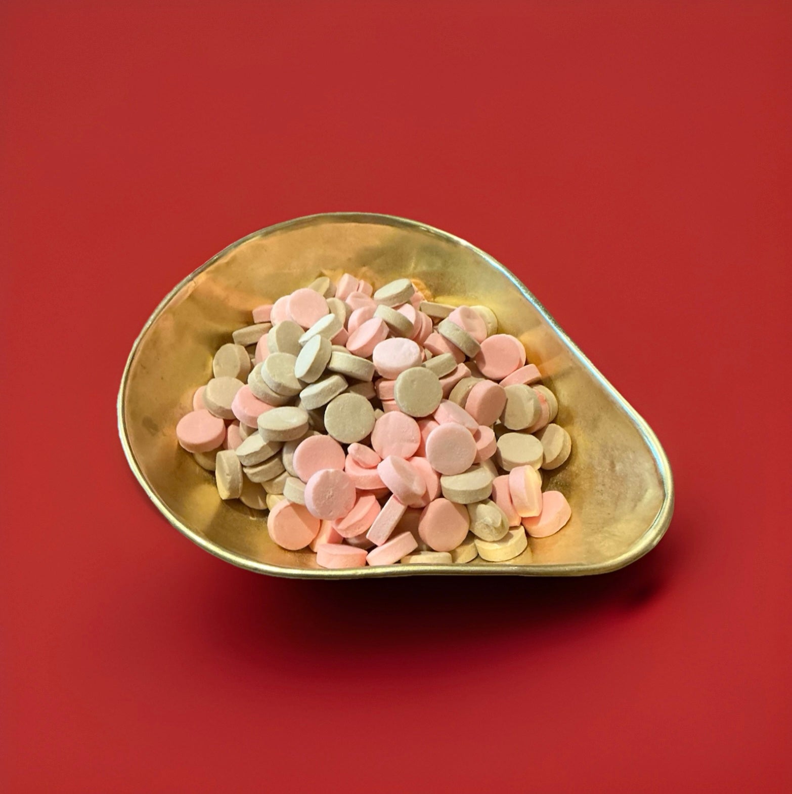Brown and pink coloured chalky discs with a floral and violet flavour in a gold bowl with a red background 