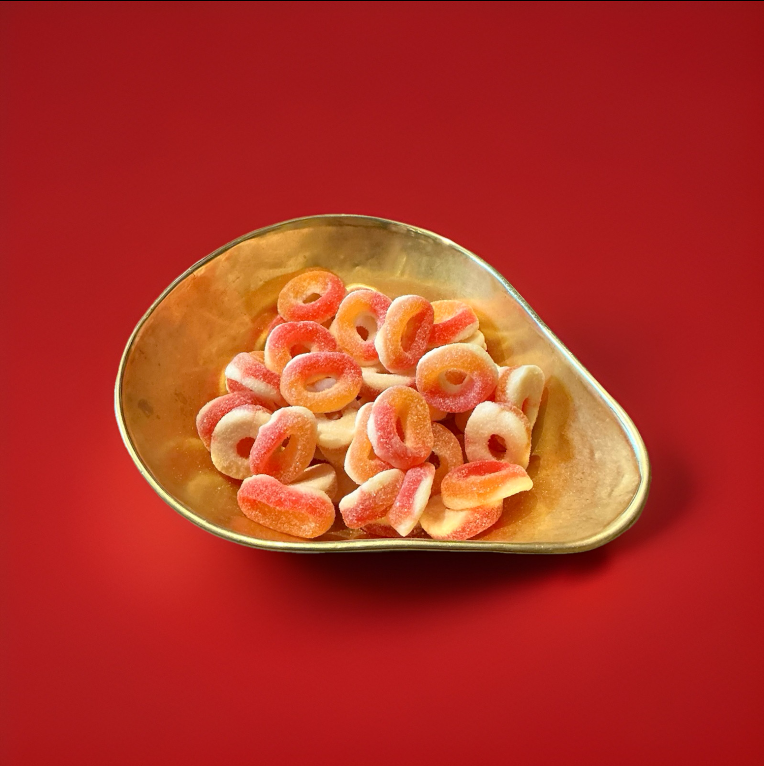 Jelly fizzy peach rings in a gold bowl with a red background 